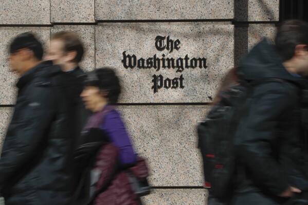 FILE - People walk by the One Franklin Square Building, home of The Washington Post newspaper, in downtown Washington on Feb. 21, 2019. The Washington Post plans to cut 240 jobs in the coming weeks through the offering of voluntary buyouts. In an email to staff, interim CEO Patty Stonesifer cited overly optimistic growth projections made in recent years. She said that the buyouts would be offered to certain jobs and departments, but didn’t specify which ones yet. (AP Photo/Pablo Martinez Monsivais, File)