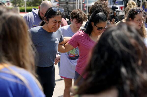 Veronica Rodriguez, left, of Dallas, becomes emotional as she gathers in a circle with others in prayer by a makeshift memorial near the mall where several people were killed in Saturday's mass shooting, Monday, May 8, 2023, in Allen, Texas. (AP Photo/Tony Gutierrez)