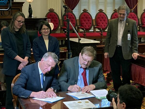 Vermont Republican Gov. Phil Scott, left, signs two amendments to the state constitution on Tuesday Dec. 13, 2022 in Montpelier, Vt. One of the amendments protects reproductive rights while the other removes what supporters say is ambiguous language and make clear that slavery and indentured servitude are prohibited in the state. Vermont voters overwhelmingly gave final approval to the amendments on Election Day last month. (AP Photo/Wilson Ring)