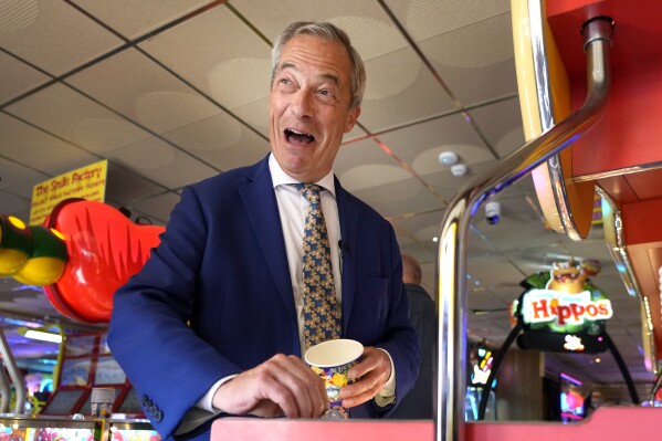 Britain's Nigel Farage, Reform UK party leader plays on a game in an amusement arcade holds out some coins whilst spending time with supporters in Clacton-On-Sea, Essex, England Friday, June 21, 2024. (AP Photo/Kirsty Wigglesworth)