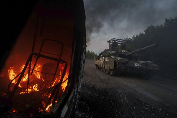 A Ukrainian tank passes by a burning car near the Russian-Ukrainian border in the Sumy region of Ukraine, Aug. 14, 2024. (AP Photo/Evgeniy Maloletka, File)