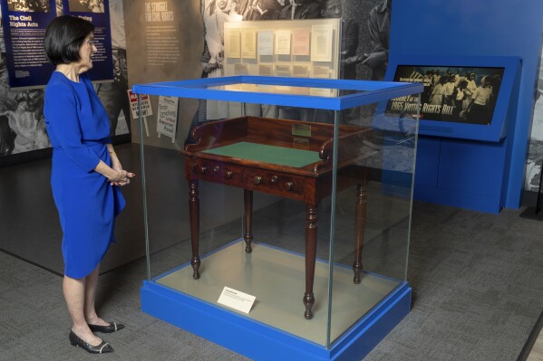 FILE - Luci Baines Johnson looks at the desk on May 16, 2023, on display at the LBJ Presidential Library, that President Lyndon B. Johnson sat at in the President's Room at the U.S. Capitol to sign the Voting Rights Act of 1965, on Aug. 6, 1965. Concern for U.S. democracy amid deep national polarization has prompted the entities supporting 13 presidential libraries dating back to Herbert Hoover to call for a recommitment to the country's bedrock principles, including the rule of law and respecting a diversity of beliefs. (AP Photo/Stephen Spillman, File)