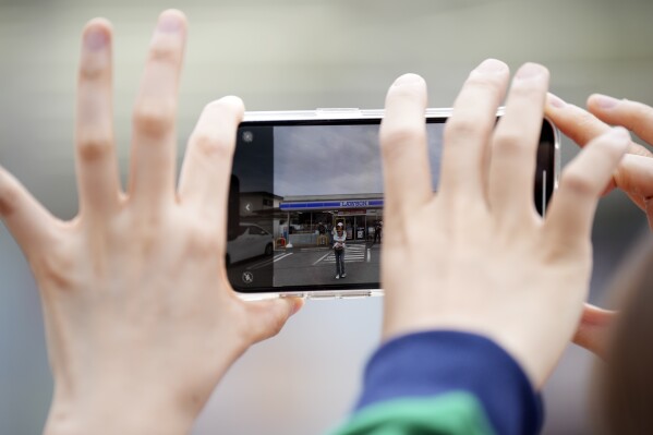 Touristen fotografieren an einem bewölkten Abend am Dienstag, dem 30. April 2024, in der Stadt Fujikawaguchiko in der Präfektur Yamanashi in Zentraljapan ein Lawson-Geschäft mit dem Berg Fuji im Hintergrund.  Die Stadt Fujikawaguchiko, die für eine Reihe beliebter Drehorte für die japanische Marke „Mount Fuji“ bekannt ist, hat am Dienstag damit begonnen, eine riesige schwarze Leinwand auf dem Bürgersteig zu platzieren, um den Blick auf den Berg in einem Viertel zu versperren, das von Japans jüngstem Fall von Übertourismus heimgesucht wird.  (AP Photo/Eugene Hoshiko)