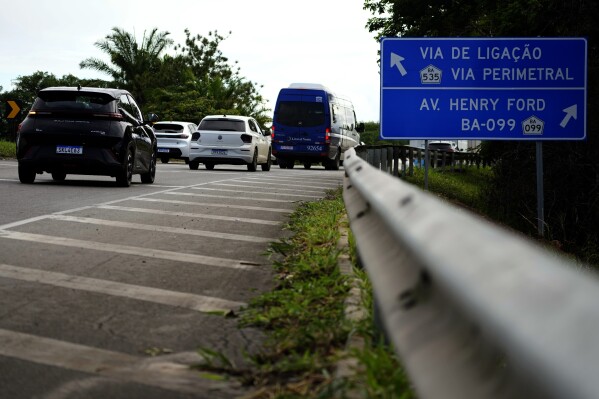 A BYD vehicle, left, passes a sign indicating Henry Ford Avenue, on the access road to the industrial complex where the BYD factory is being built, in Camacari, Bahia state, Brazil, Thursday, March 6, 2025. (AP Photo/Eraldo Peres)