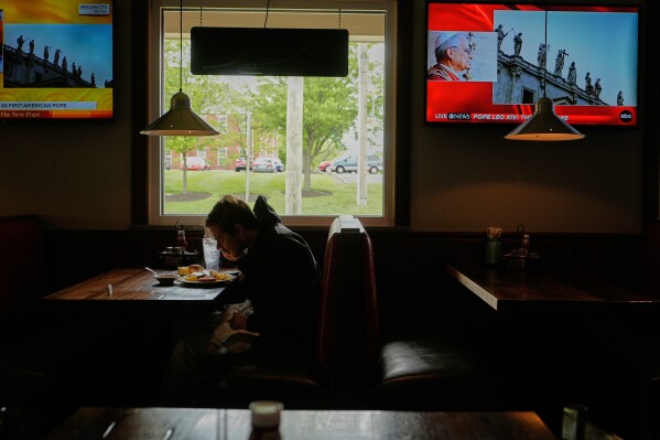 A patron eats lunch as live coverage of the newly elected Pope Leo XIV from St. Peter's Basilica at the Vatican is on televisions at Ron's Roost Chicken Restaurant, Thursday, May 8, 2025, in Cincinnati. (AP Photo/Carolyn Kaster)