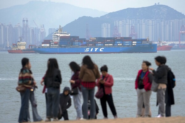File - A container ship passes tourists in Xiamen in southeast China's Fujian province on Dec. 26, 2023. Hobbled by high interest rates, persistent inflation, slumping trade and a diminished China, the global economy will slow for a third consecutive year in 2024. (AP Photo/Andy Wong, File)