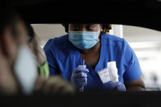 Healthcare worker Rahaana Smith instructs passengers how to use a nasal swab, Friday, July 24, 2020, at a drive-thru COVID-19 testing site at the Miami-Dade County Auditorium, in Miami. Florida has experienced a sharp increase in coronavirus deaths over the past two weeks, including another 136 recorded Friday as the state's total confirmed cases topped 400,000. (AP Photo/Wilfredo Lee)