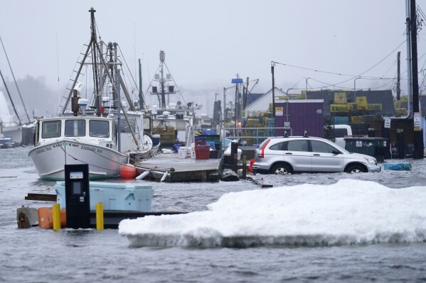 FILE - A car sits in a flooded parking lot at Widgery Wharf in this Jan. 10, 2024, in Portland, Maine. Maine's government is making tens of millions of dollars available to rebuild the state's working waterfront communities after a series of devastating winter storms pummeled the state's docks, wharfs and coastal businesses. (AP Photo/Robert F. Bukaty)