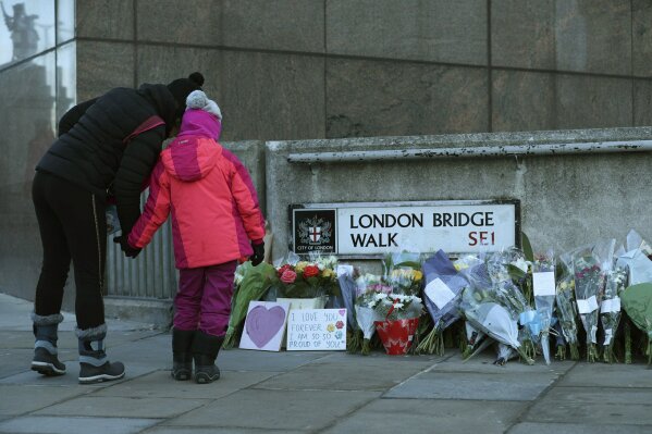 Passers-by stop to look at flowers left at London Bridge following the attack on Friday, in London, Monday, Dec. 2, 2019. London Bridge reopened to cars and pedestrians Monday, three days after a man previously convicted of terrorism offenses stabbed two people to death and injured three others before being shot dead by police. (Yui Mok/PA via AP)