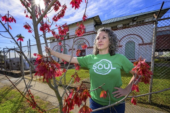 Susannah Burley, founding director of SOUL (Sustaining Our Urban Landscape), stands by a tree the organization previously planted in front of New Orleans Sewerage and Water Board pumping station in the Algiers neighborhood of New Orleans, Thursday, Feb. 27, 2025. (AP Photo/Matthew Hinton)