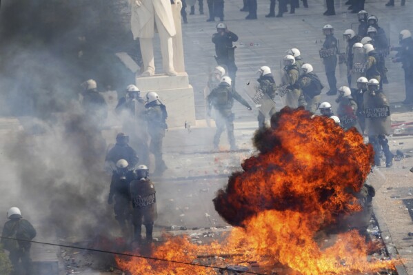 Riot police try to avoid the flames from a petrol bomb outside from the parliament during a rally in central Athens, Greece to mark two years since a deadly rail disaster that has also triggered hundreds of other demonstrations and a general strike, on Friday, Feb. 28, 2025. (AP Photo/Thanassis Stavrakis)