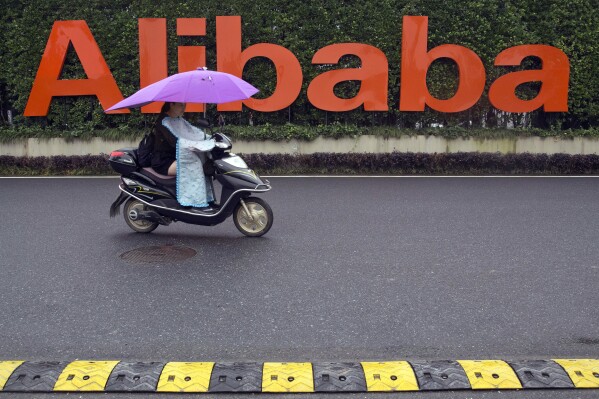 FILE - A woman rides a scooter past the company logo outside the Alibaba Group headquarters in Hangzhou, in eastern China's Zhejiang province, May 27, 2016. Shares of Chinese e-commerce firm Alibaba Group Holding plunged as much as 10% in New York after it said Thursday, Nov. 16, 2023, that plans to spin off its cloud business were scrapped, citing uncertainties due to U.S. chip restrictions. (AP Photo/Ng Han Guan, File)