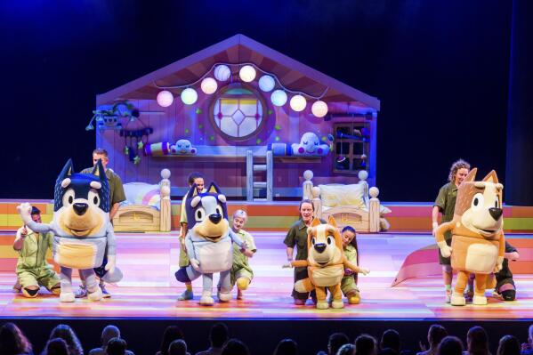 This image shows characters, from left, Bandit, Bluey,  Bingo and Chili and their puppeteers during a performance of “Bluey’s Big Play." The theatrical adaptation of the popular animated children’s TV show “Bluey” starts a multistate tour this month. (Darren Thomas via AP)