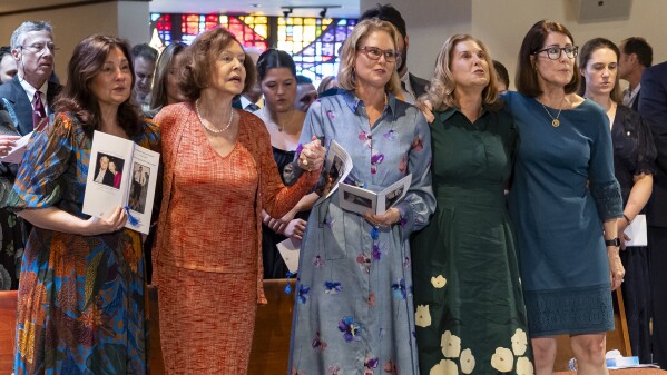 Adele Graham, wife of U.S. Sen. and two-term Florida Gov. Bob Graham, second from left, stands with her daughters, from left to right, Kendall Graham, Suzanne Graham Gibson, Cissy Graham McCullough and Gwen Graham as they sing "God Bless America," during the public celebration of life service for Bob Graham at the Miami Lakes United Church of Christ, Saturday, May 11, 2024, in Miami Lakes, Fla. Graham died in April at the age of 87. (Matias J. Ocner/Miami Herald via AP, Pool)