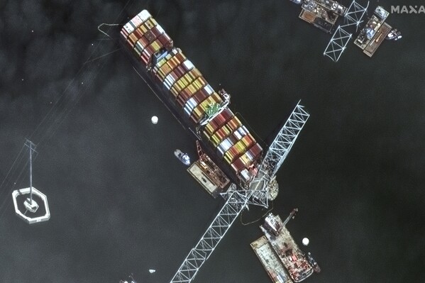 This satellite image provided by Maxar shows the bow of the container ship Dali remains stuck underneath sections of the fallen Francis Scott Key Bridge, while salvage crews and barges with cranes continue removing some of the bridge debris and hundreds of shipping containers still onboard the vessel, in Baltimore, Monday, April 8, 2024. (Satellite image ©2024 Maxar Technologies via AP)