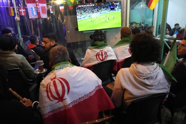 Lebanese soccer fans of Iran's team cover their backs with Iranian flags, as they sit at a coffee shop smoking water pipes and watch the World Cup group B soccer match between Iran and the United States, in the Hezbollah stronghold in the southern suburbs of Beirut, Lebanon, Tuesday, Nov. 29, 2022. (AP Photo/Hussein Malla)