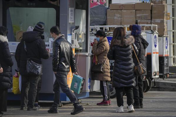 Residents wait in line for their routine COVID-19 throat swabs near tricycle carts loaded with goods in Beijing, Wednesday, Dec. 7, 2022. China's imports and exports shrank in November as global demand weakened and anti-virus controls weighed on the second-largest economy. (AP Photo/Andy Wong)
