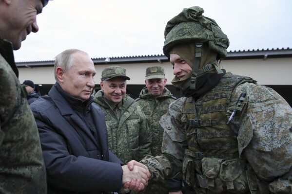 FILE - Russian President Vladimir Putin shakes hands with a soldier and Russian Defense Minister Sergei Shoigu stands next to him, smiling, during a visit at a military training centre of the Western Military District in Ryazan Region, Russia on Oct. 20, 2022. Putin begins his fifth term as Russian president in an opulent Kremlin inauguration on Tuesday after destroying his political opposition, launching a devastating war in Ukraine and consolidating power. (Mikhail Klimentyev, Sputnik, Kremlin Pool Photo via AP, File)