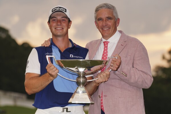 Viktor Hovland, of Norway, left, celebrates winning the Tour Championship golf tournament with the FedEx Cup trophy with Jay Monahan, commissioner of the PGA, on the 18th green, Sunday, Aug. 27, 2023, in Atlanta. (AP Photo/John Bazemore)