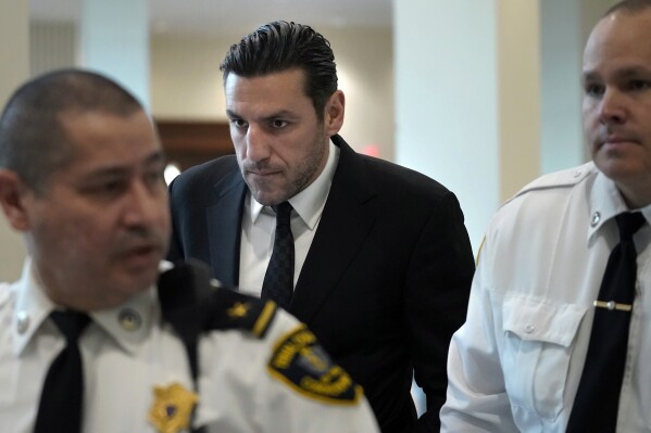 Boston Bruins forward Milan Lucic, center, is flanked by court officers as he arrives at Boston Municipal Court in Boston, Tuesday, Nov. 21, 2023, for his arraignment on an assault charge in connection with his arrest over the weekend after his wife called police to their home and said he tried to choke her. Lucic was released on personal recognizance bail Tuesday after pleading not guilty to assaulting his wife. (AP Photo/Steven Senne)