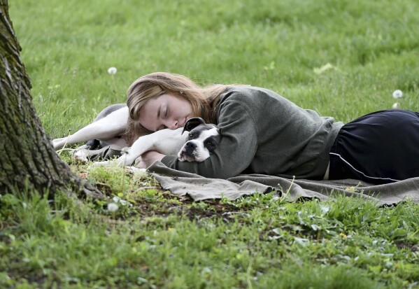 FILE -A woman and her dog nap between rain showers at Schenley Park, Tuesday, May 4, 2021 in Pittsburgh. The Gallup survey, released Monday, April 15, 2024, says that a majority of Americans say they would feel better if they could have more sleep. But in the U.S., where the ethos of grinding and pulling yourself up by your own bootstraps is ubiquitous, getting enough sleep can seem like a dream.(Pam Panchak/Pittsburgh Post-Gazette via AP, File)