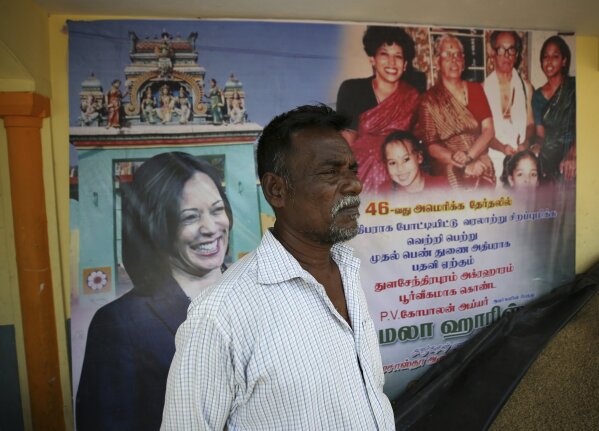 An Indian villager stands in front of a banner displaying photographs of U.S. Vice President-elect Kamala Harris in Thulasendrapuram, the hometown of Harris' maternal grandfather, south of Chennai, Tamil Nadu state, India, Tuesday, Jan. 19, 2021. The inauguration of President-elect Joe Biden and Vice President-elect Kamala Harris is scheduled be held Wednesday. (AP Photo/Aijaz Rahi)