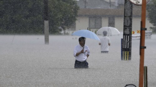 People wade through a street due to a heavy rain in Kurume, Fukuoka prefecture, southern Japan Monday, July 10, 2023. Scientists have long warned that more extreme rainfall is expected in a warming world. (Kyodo News via AP)