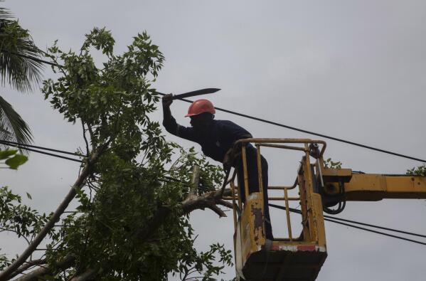An electric company worker mounted on a crane uses a machete to cut away tree branches felled on power lines in the wake of Hurricane Ian in Havana, Cuba, Wednesday, Sept. 28, 2022. Cuba remained in the dark early Wednesday after Ian knocked out its power grid and devastated some of the country's most important tobacco farms when it hit the island's western tip as a major storm. (AP Photo/Ismael Francisco)