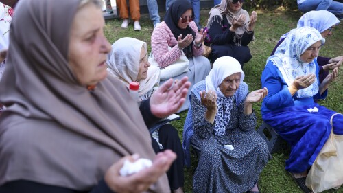 Muslim women pray in Visoko, Bosnia, Sunday, July 9, 2023 next to a truck carrying 30 coffins with remains of the recently identified victims of the 1995 Srebrenica genocide. So far, the remains of more than 6,600 people have been found and buried at a vast and ever-expanding memorial cemetery in Potocari, outside Srebrenica. (AP Photo/Armin Durgut)