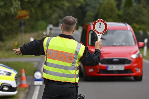 A police officer stops a car during a check against smuggling during the police's efforts to combat smuggling and illegal immigration, in Roggosen, Germany, Monday, Sept. 25, 2023. More than 350 German federal police searched premises across the country in connection with smuggling of migrants early on Tuesday. (Patrick Pleul/dpa via AP)