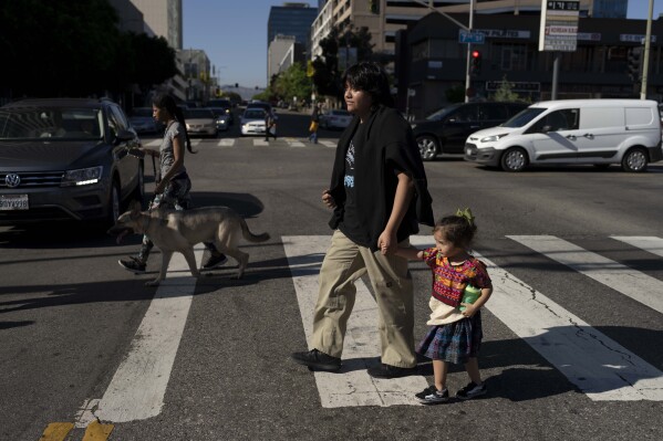 Deneffy Sánchez and his little sister, Jennifer, hold hands as they cross the street to get cold drinks in Los Angeles, Tuesday, Aug. 29, 2023. Like Deneffy, more than a quarter of U.S. students have missed at least 10 percent of the school year since schools reopened making it harder for them to catch up after the pandemic. In Los Angeles, housing insecurity is one of the biggest reasons kids have missed school. (AP Photo/Jae C. Hong)