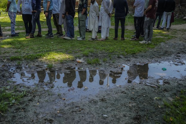 People standing in a queue to cast vote outside the polling booth are reflected in a puddle during the fifth round of multi-phase national elections in Sumbal north of Srinagar, Indian controlled Kashmir, Monday, May 20, 2024. (AP Photo/Mukhtar Khan)