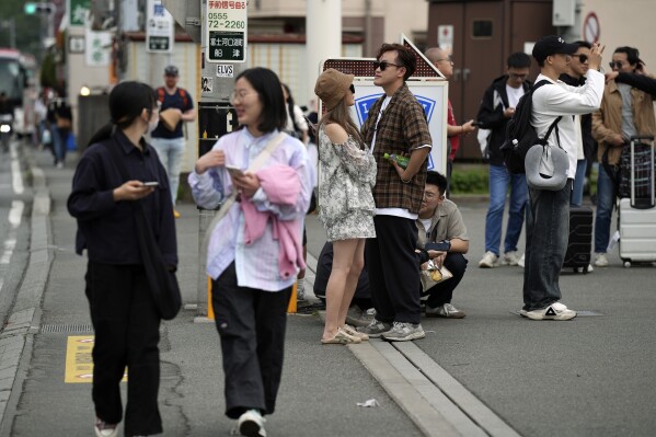 Touristen tummeln sich am Dienstagabend, dem 30. April 2024, vor Lawson's Convenience Store, einem beliebten Fotospot mit einem atemberaubenden Blick auf den Berg Fuji im Hintergrund, in der Stadt Fujikawaguchiko, Präfektur Yamanashi, Zentraljapan.  Die Stadt Fujikawaguchiko, die für eine Reihe berühmter Drehorte für die japanische Marke „Mount Fuji“ bekannt ist, hat am Dienstag damit begonnen, eine riesige schwarze Leinwand entlang des Bürgersteigs zu platzieren, um den Blick auf den Berg in einem Viertel zu versperren, das von Japans jüngstem Fall von Übertourismus heimgesucht wurde.  (AP Photo/Eugene Hoshiko)