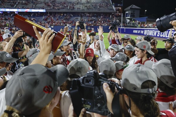 Oklahoma coach Patty Gasso, hand raised, with white sleeve, celebrates with the team after a win over Texas in the NCAA Women's College World Series softball championship series Thursday, June 6, 2024, in Oklahoma City. (AP Photo/Alonzo Adams)