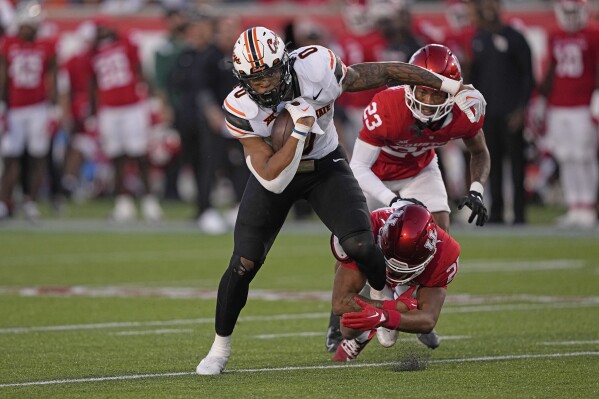 Houston defensive back Juwon Gaston (21) tries to tackle Oklahoma State running back Ollie Gordon II (0) during the second half of an NCAA college football game Saturday, Nov. 18, 2023, in Houston. Oklahoma State won 43-30. (AP Photo/David J. Phillip)