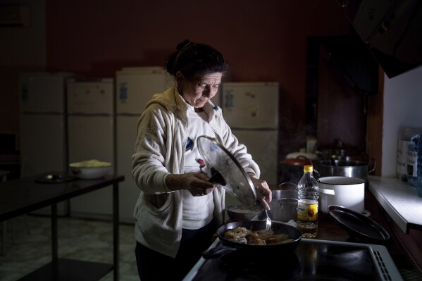 Natalia Zhyvohliad, an internally displaced person from Nova Petrivka in the Zaporizhzhia region of Ukraine, fries fish for her children at the IDP shelter in Kyiv, on Friday, Jan. 19, 2024. (AP Photo/Evgeniy Maloletka)