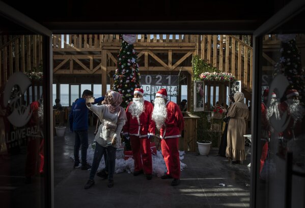 Palestinians take a selfie with waiters dressed as Santa Clause in a restaurant on the beach in Gaza City, Sunday Dec. 13, 2020. (AP Photo/Khalil Hamra)