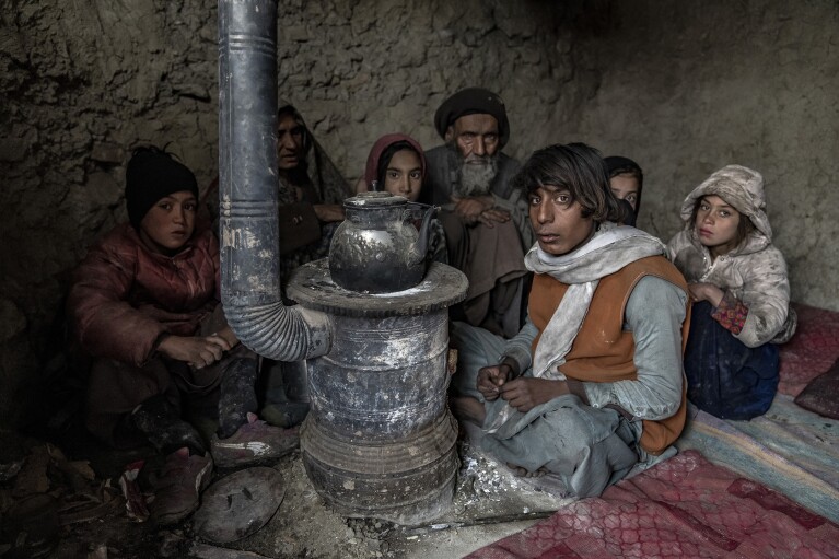 An internally displaced family huddle by a stove lit by burning garbage to keep warm in a camp on the outskirts of Kabul, Afghanistan, Sunday, Jan. 29, 2023. (AP Photo/Ebrahim Noroozi)