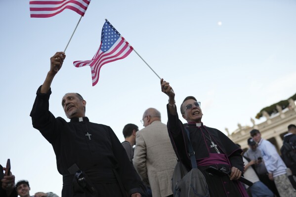 Clerics wave US flags during the speech of the newly elected Pope Leo XIV at the Vatican, Thursday, May 8, 2025. (AP Photo/Francisco Seco)