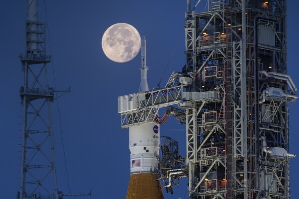 A full moon is seen behind the Artemis I Space Launch System (SLS) and Orion spacecraft, atop the mobile launcher, are prepared for a wet dress rehearsal to practice timelines and procedures for launch, at Launch Complex 39B at NASA's Kennedy Space Center in Florida on June 14, 2022. On Tuesday, Jan. 9, 2024, NASA said astronauts will have to wait until 2025 before flying to the moon and another few years before landing on it. (Cory Huston/NASA via AP)