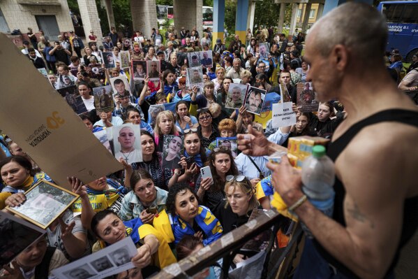 People show photos of their missed relatives to Ukrainian soldiers during a POWs exchange between Russia and Ukraine, in Chernyhiv region, Ukraine, Saturday, May 24, 2025. (AP Photo/Evgeniy Maloletka)