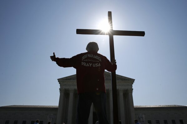 Tom Alexander holds a cross as he prays prior to rulings outside the Supreme Court on Capitol Hill in Washington, Wednesday, July 8, 2020. The Supreme Court is siding with two Catholic schools in a ruling that underscores that certain employees of religious schools, hospitals and social service centers can’t sue for employment discrimination. (AP Photo/Patrick Semansky)