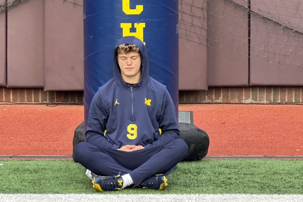Michigan quarterback J.J. McCarthy sits on the field with his back against a padded goalpost on Nov. 4, 2023 in Ann Arbor, Mich. McCarthy meditates roughly two hours before games. This week, amid a sign-stealing saga and a matchup with rival Ohio State, keeping his mind free from distractions is paramount. (AP Photo/Larry Lage)