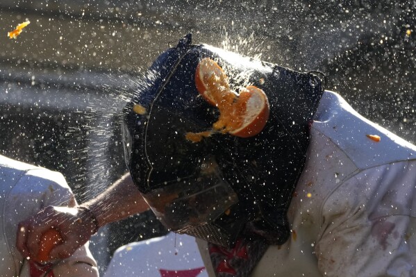 People wearing protection helmets and costumes pelt each other with oranges during the "Battle of the Oranges" part of Carnival celebrations in the northern Italian Piedmont town of Ivrea, Italy, Tuesday, Feb. 13, 2024. (AP Photo/Antonio Calanni)