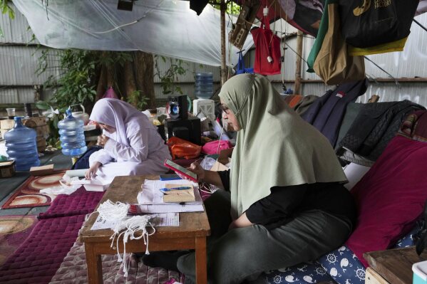 Nina Herlina, right, checks her mobile phone as she waits for customer with her daughter Camelia, at her livestock stall in Jakarta, Indonesia, Monday, June 2, 2025. (AP Photo/Achmad Ibrahim)
