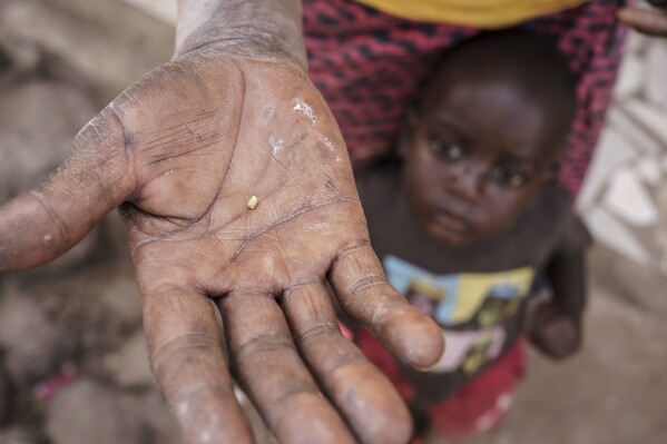 Sadio Camara's son clings to her as she holds a crumb of gold she extracted using mercury at her home in the Kedougou region of Senegal on Thursday, Jan. 16, 2025. (AP Photo/Annika Hammerschlag)