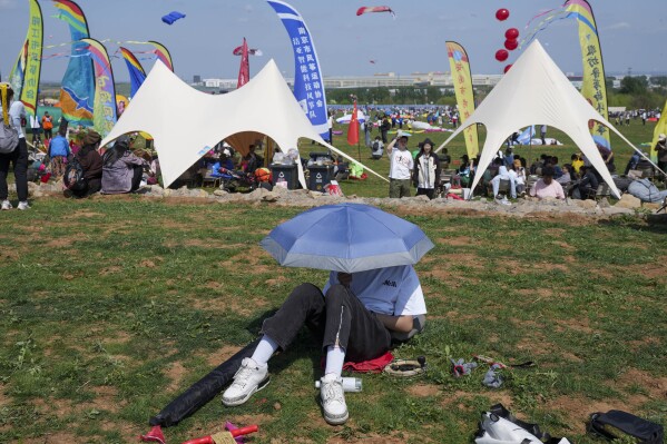 A visitor rests in the shade of an umbrella during the 41st International Kite Festival in Weifang, Shandong Province of China, Saturday, April 20, 2024. (AP Photo/Tatan Syuflana)