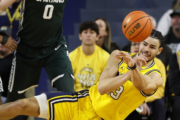 Michigan forward Olivier Nkamhoua (13) passes the ball while defended by Michigan State forward Jaxon Kohler (0) during the first half of an NCAA college basketball game Saturday, Feb. 17, 2024, in Ann Arbor, Mich. (AP Photo/Duane Burleson)