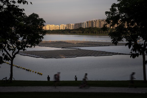 Joggers pass by a floating solar panel farm on the Bedok Reservoir lined by apartment buildings in Singapore, Sunday, July 16, 2023. (AP Photo/David Goldman)