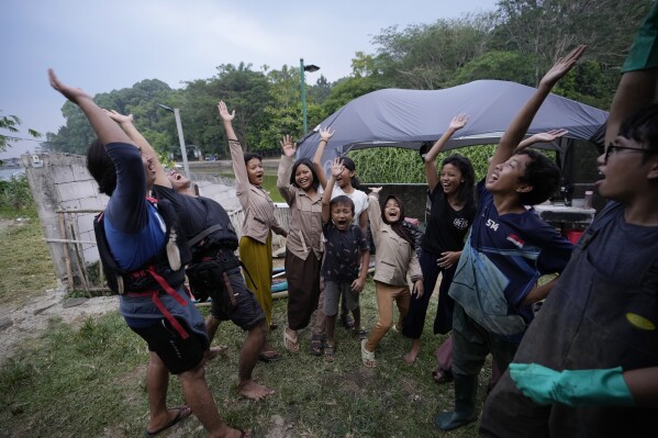 Environmental activists of Situ Gede Cleanliness Warrior cheer after they pick up trash at Setu Gede lake in Bogor, West Java, Indonesia, Tuesday, Oct. 10, 2023. Young people have been at the forefront of environmental and climate change movements in the recent years: initiatives like school strikes for climate action, protests at United Nations climate talks and around the world and local clean ups have often been youth-led. (AP Photo/Achmad Ibrahim)